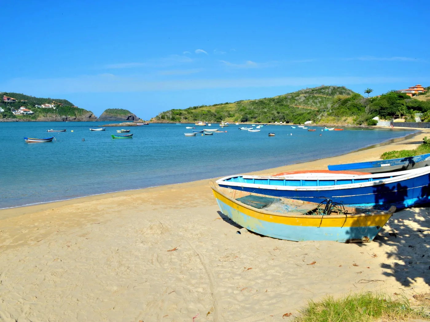 Barcos de pesca coloridos na areia da Praia da Ferradura, em Búzios, com ilhotas ao fundo