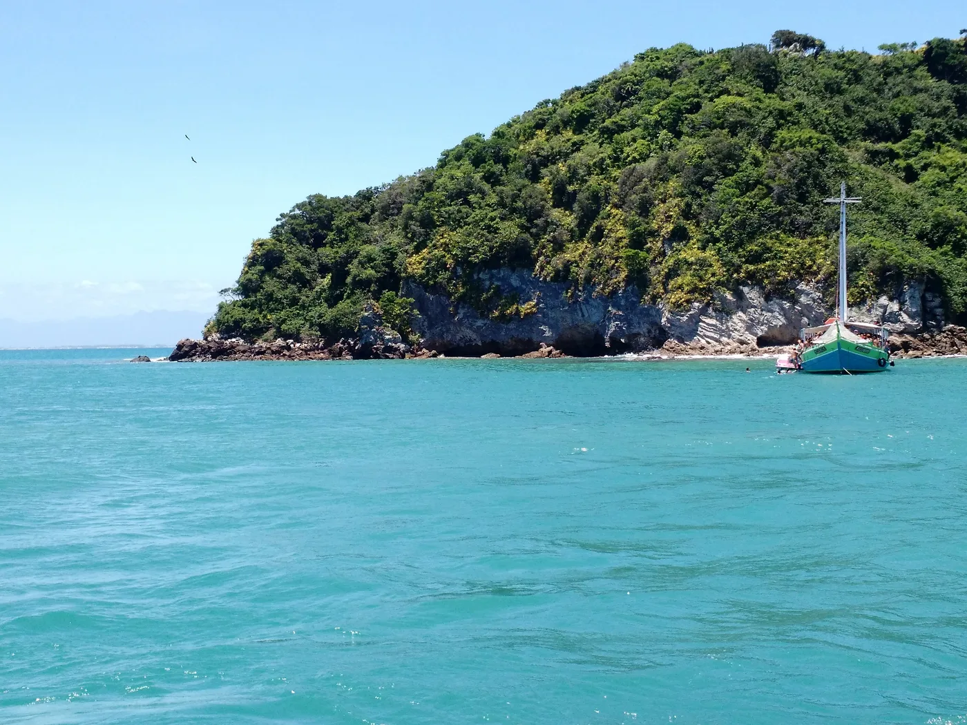 Ilha Feia, em Búzios, coberta de mata e cercada de água turquesa, com um barco ancorado