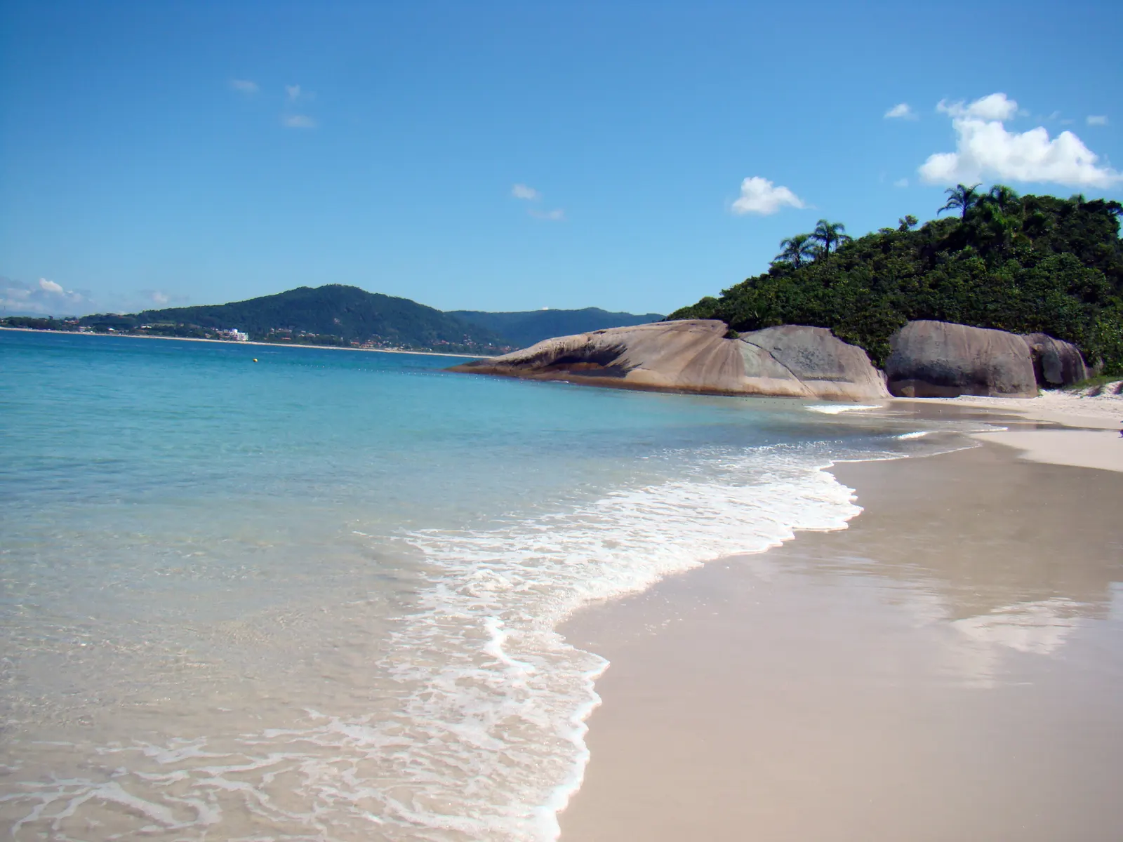 Faixa de areia branca e água transparente na Ilha do Campeche, com o costão de pedra ao fundo