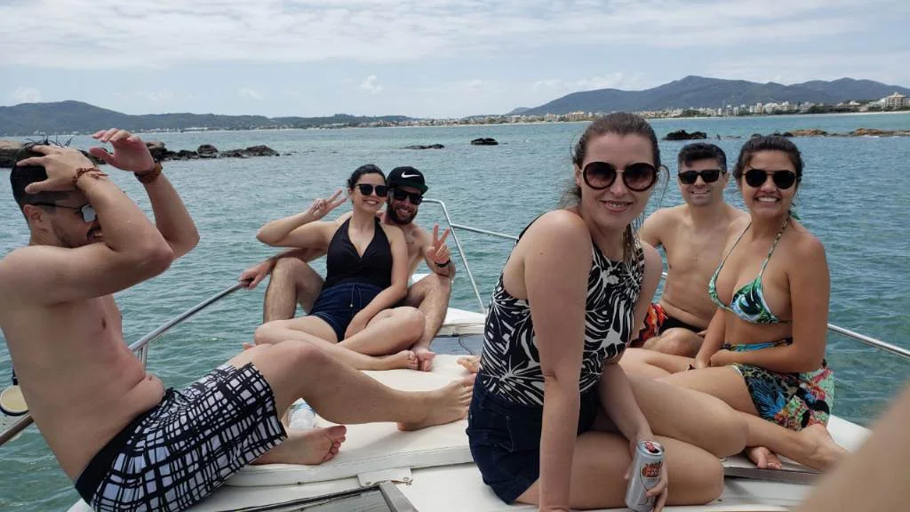 Grupo de amigos sentado na proa de uma lancha, com a orla de Florianópolis ao fundo