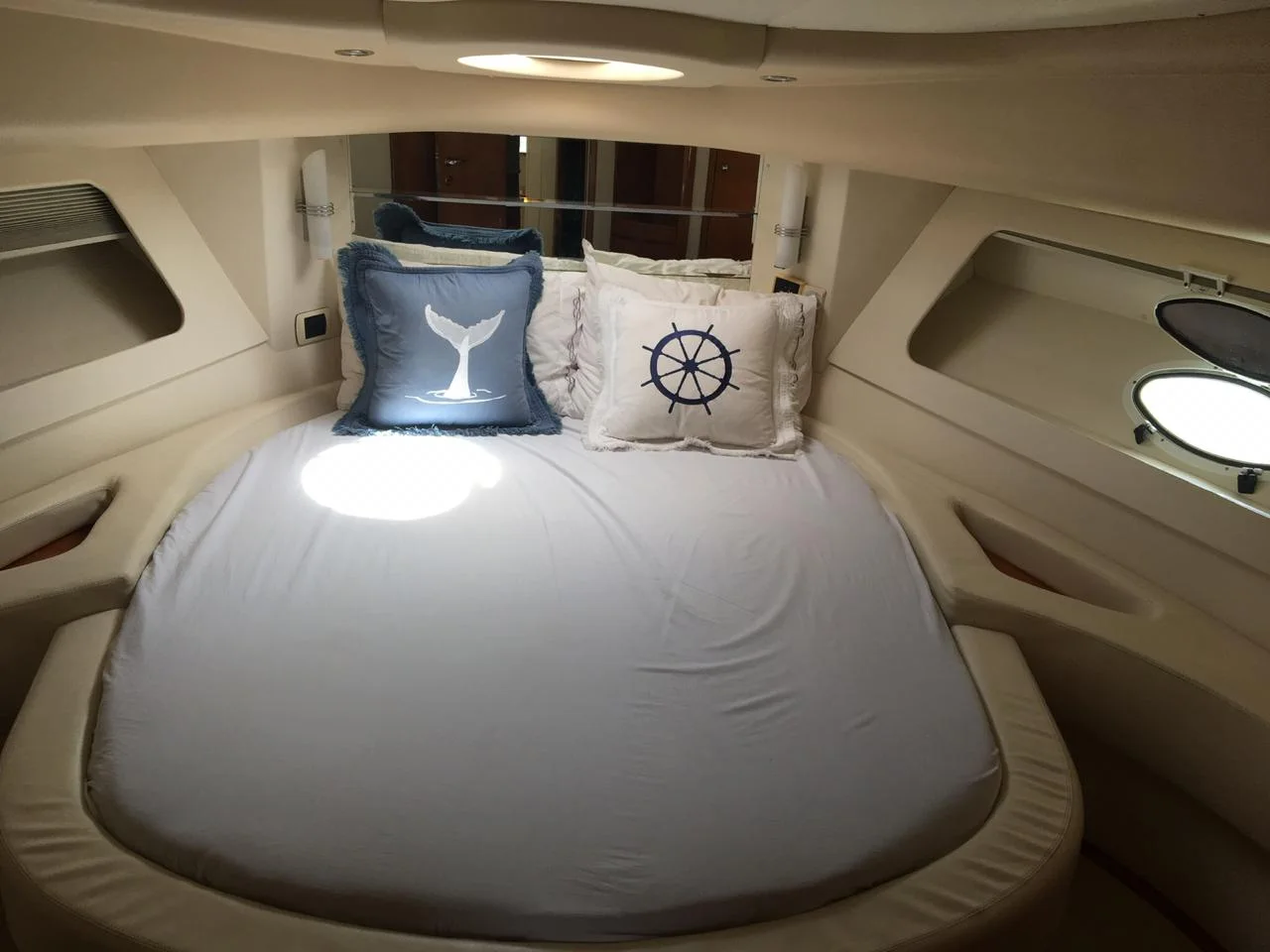 Cabine do iate com cama de casal arrumada e almofadas náuticas