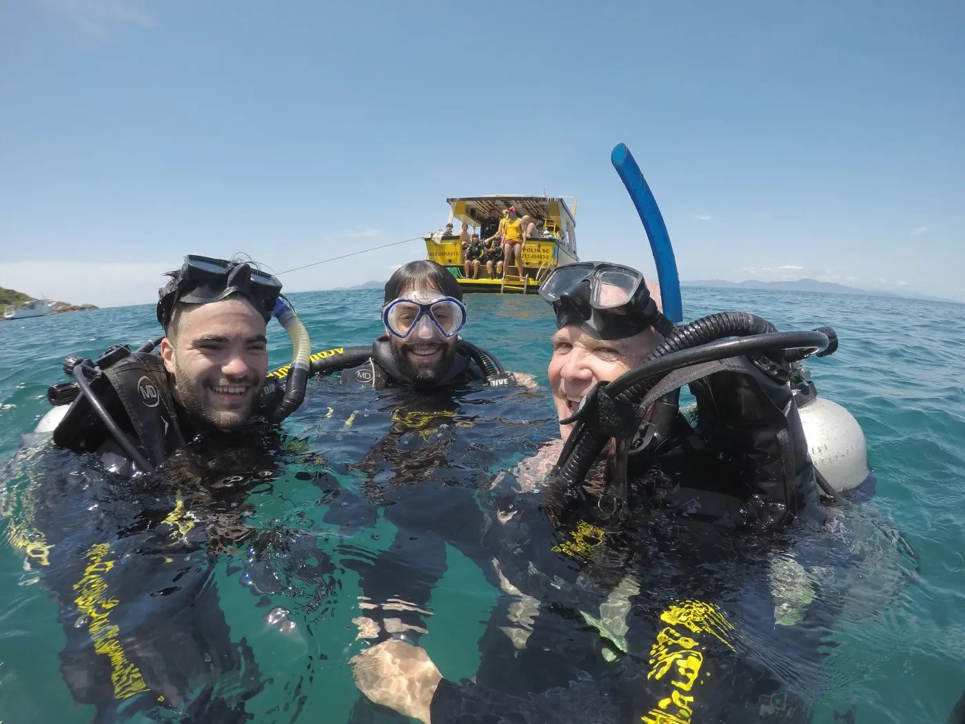 Três mergulhadores sorrindo na superfície com a embarcação Acquanauta ao fundo