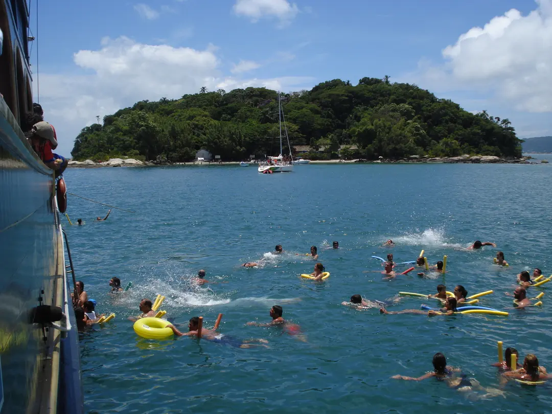Passageiros nadando ao lado do barco, com a Ilha do Francês ao fundo
