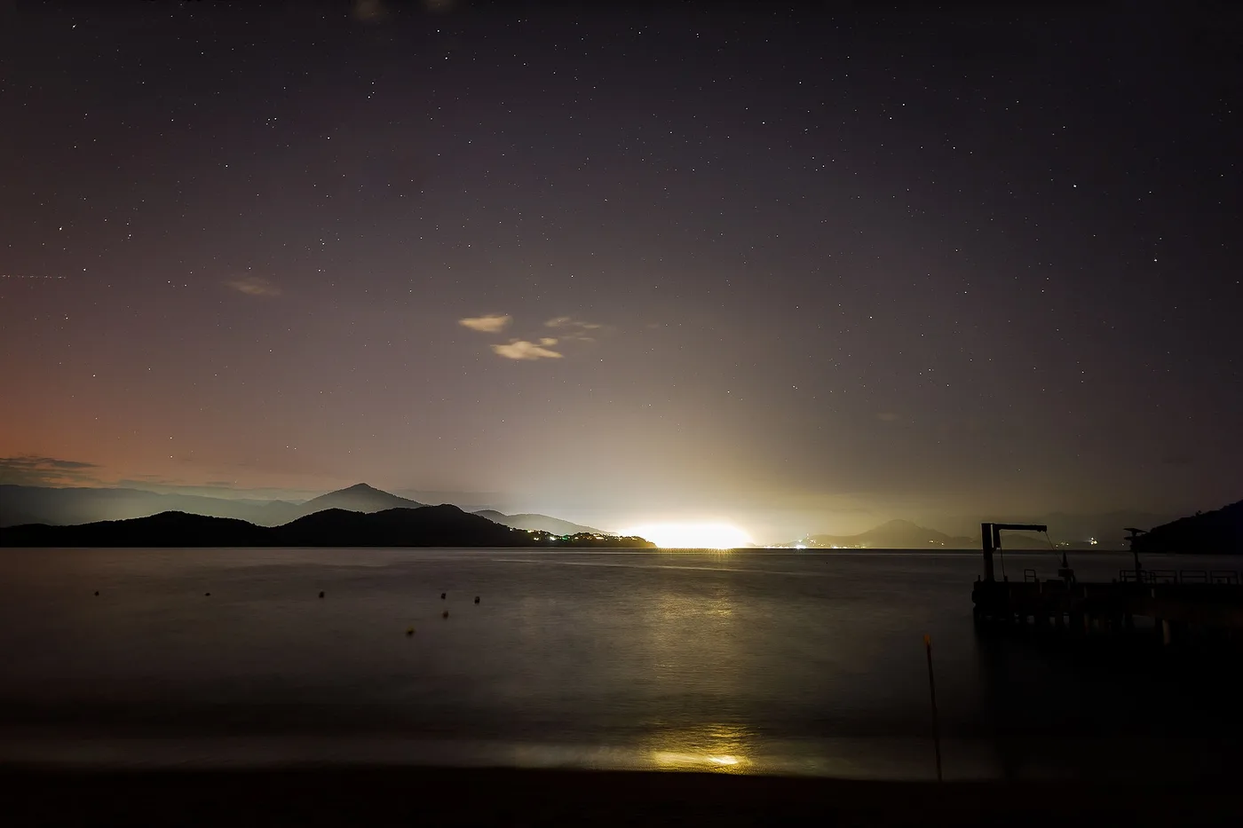 Céu noturno estrelado sobre o Parque Estadual da Ilha Anchieta, com a silhueta da mata no horizonte