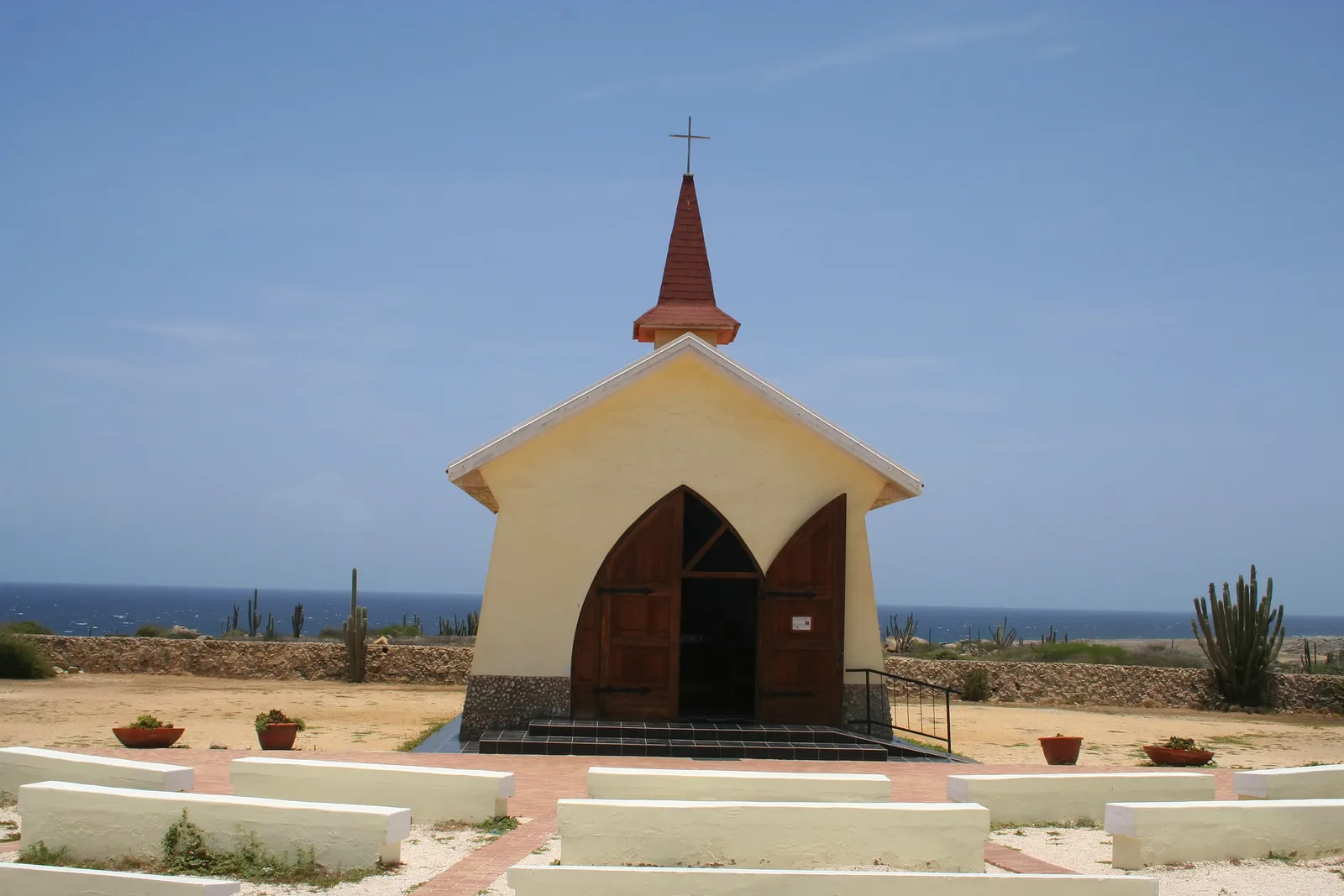 Capela amarela de Alto Vista entre cactos, com o mar ao fundo, em Aruba