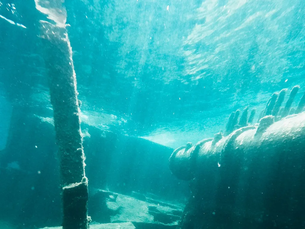 Estrutura submersa coberta de vida marinha, com raios de luz ao fundo do mar