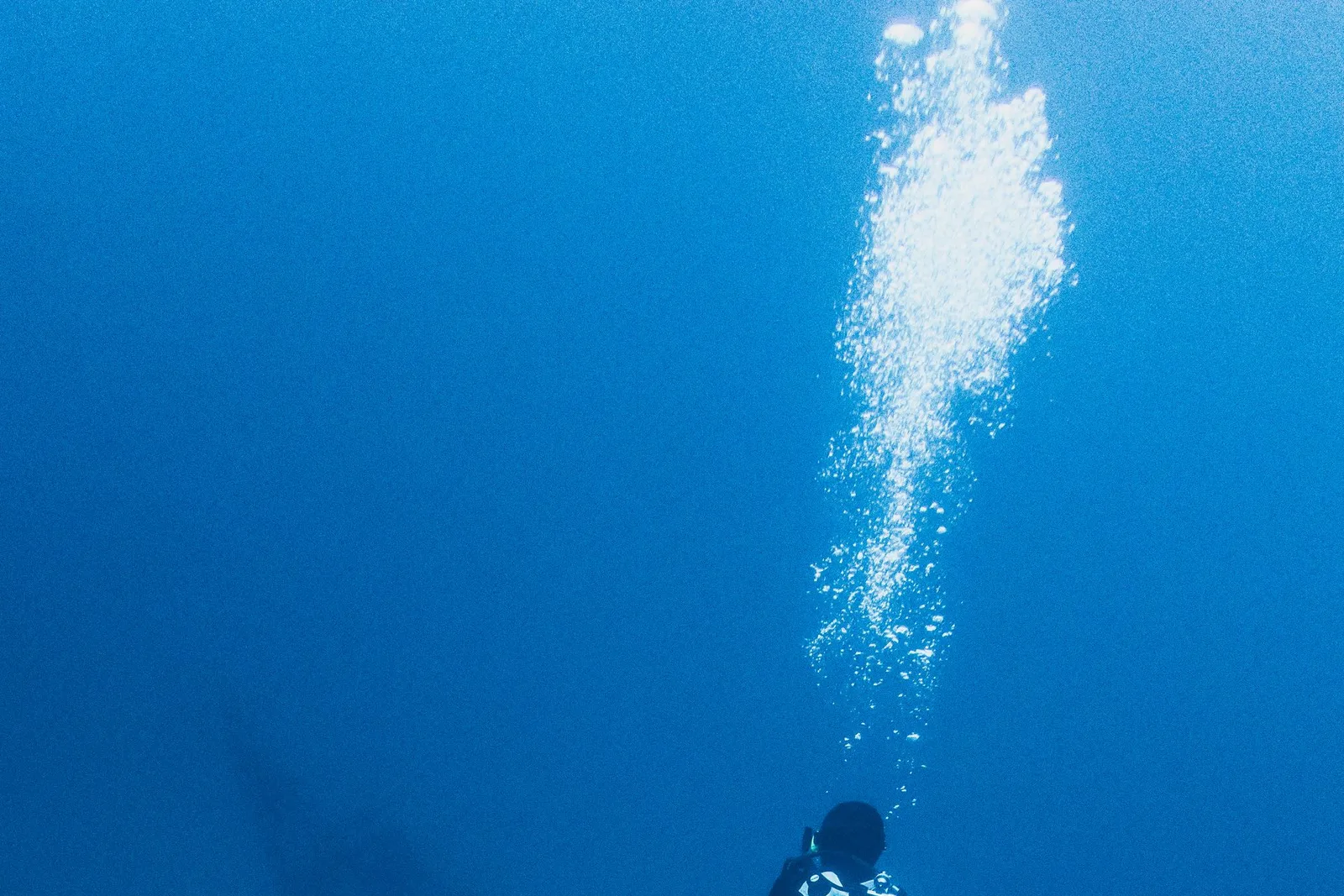Mergulhador descendo em direção ao fundo azul, com trilha de bolhas