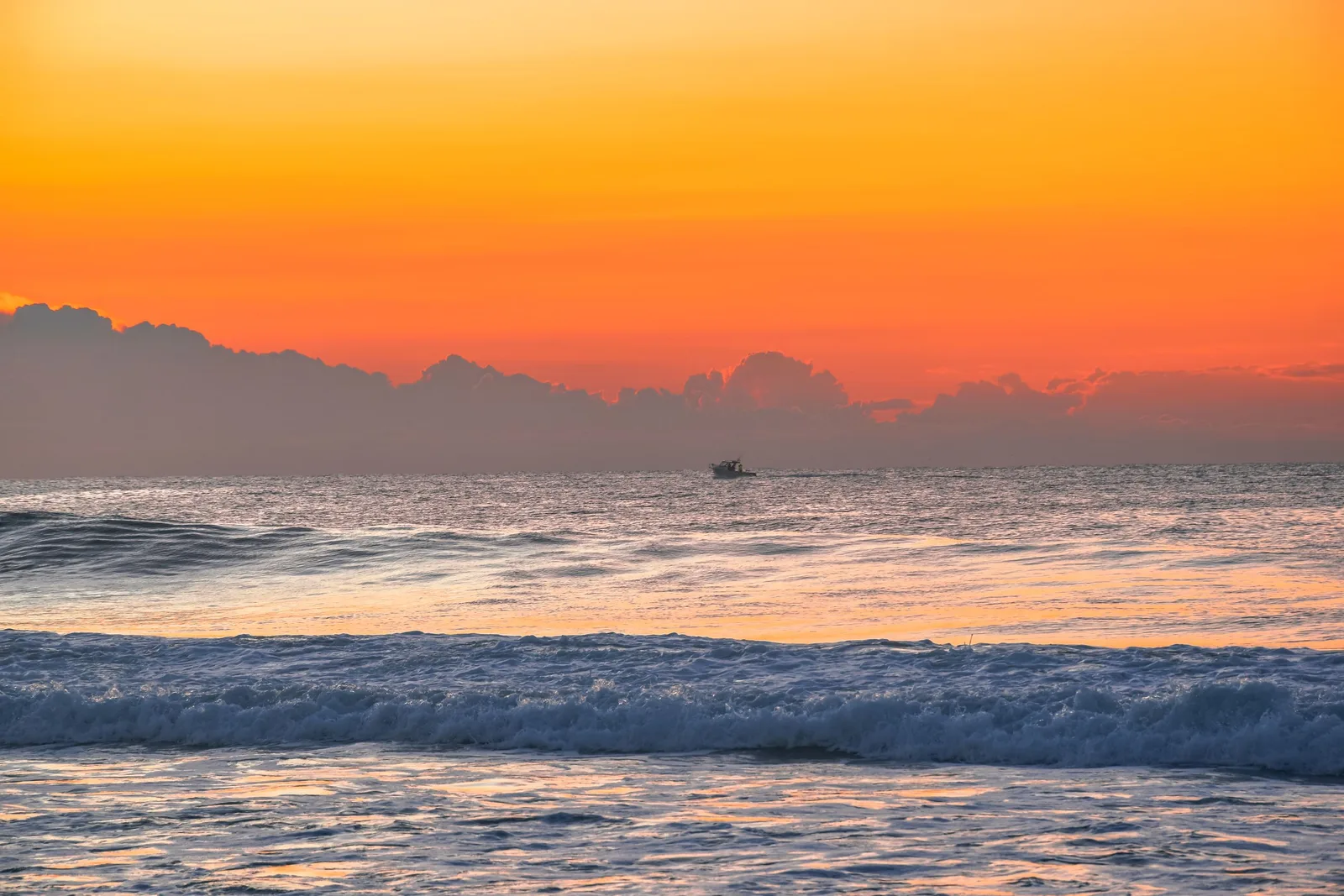 Barco de pesca em silhueta contra o pôr do sol no oceano