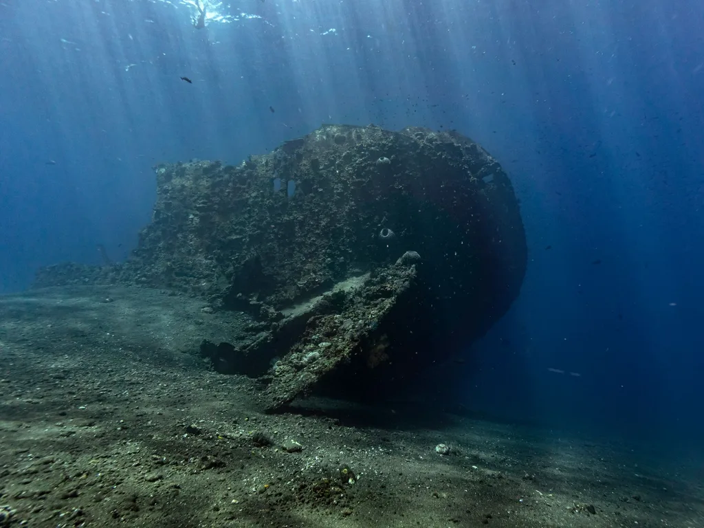 Casco de navio naufragado sobre fundo de areia, iluminado por raios de sol