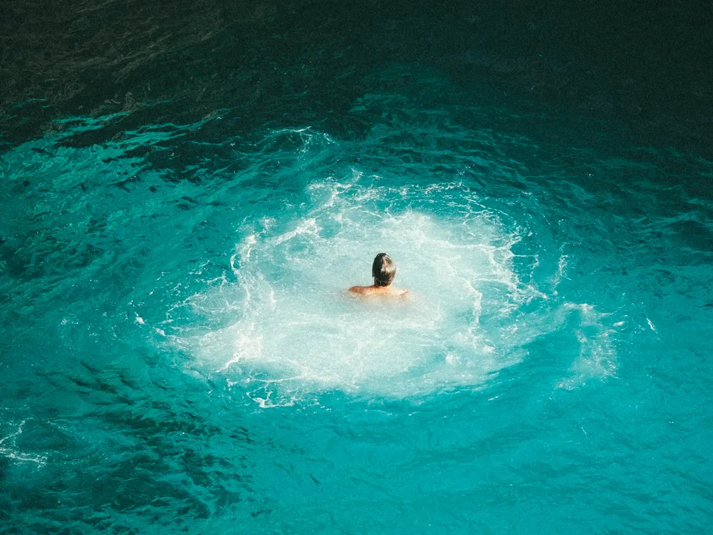 Banhista no mar azul-turquesa aos pés dos penhascos do Rick's Café, em Negril