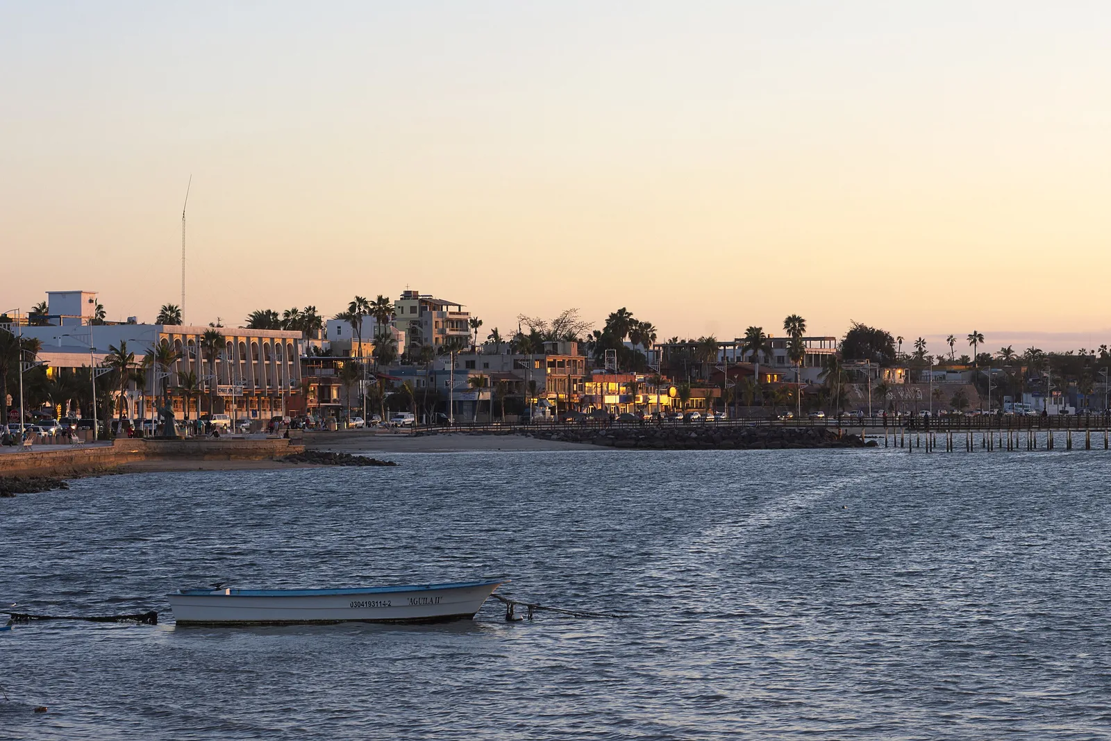 Malecón de La Paz ao entardecer, com um barco de pesca na baía