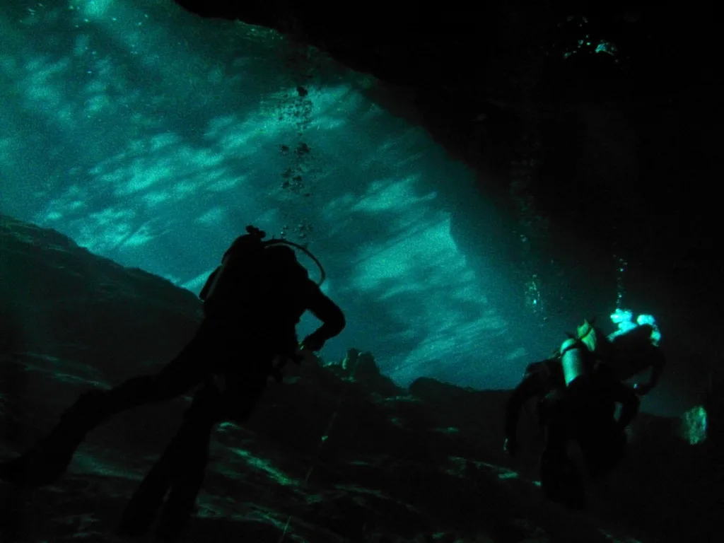 Mergulhadores na zona de luz do cenote Chac Mool, com os feixes de sol entrando pela abertura