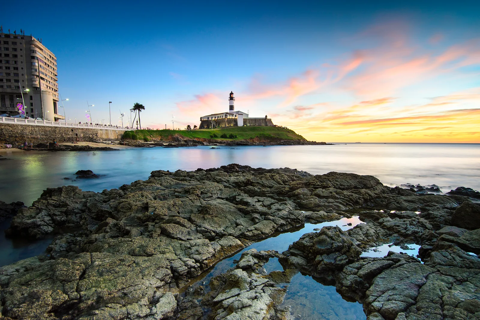 Farol da Barra ao entardecer, com o céu alaranjado sobre o mar, em Salvador