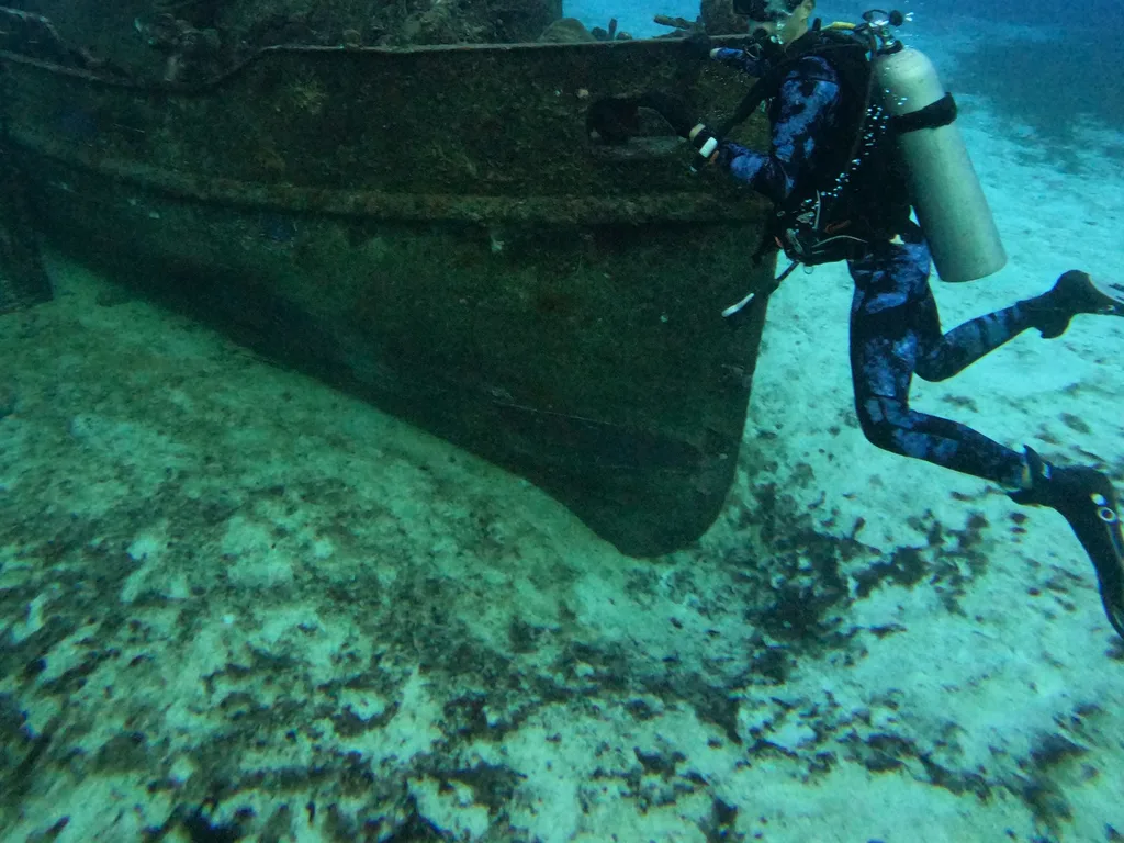 Mergulhador junto ao casco de um barco afundado sobre a areia